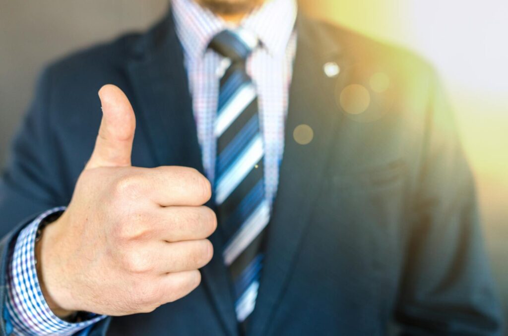 Close-up of a businessman in a suit giving a thumbs-up in a bright, positive setting.